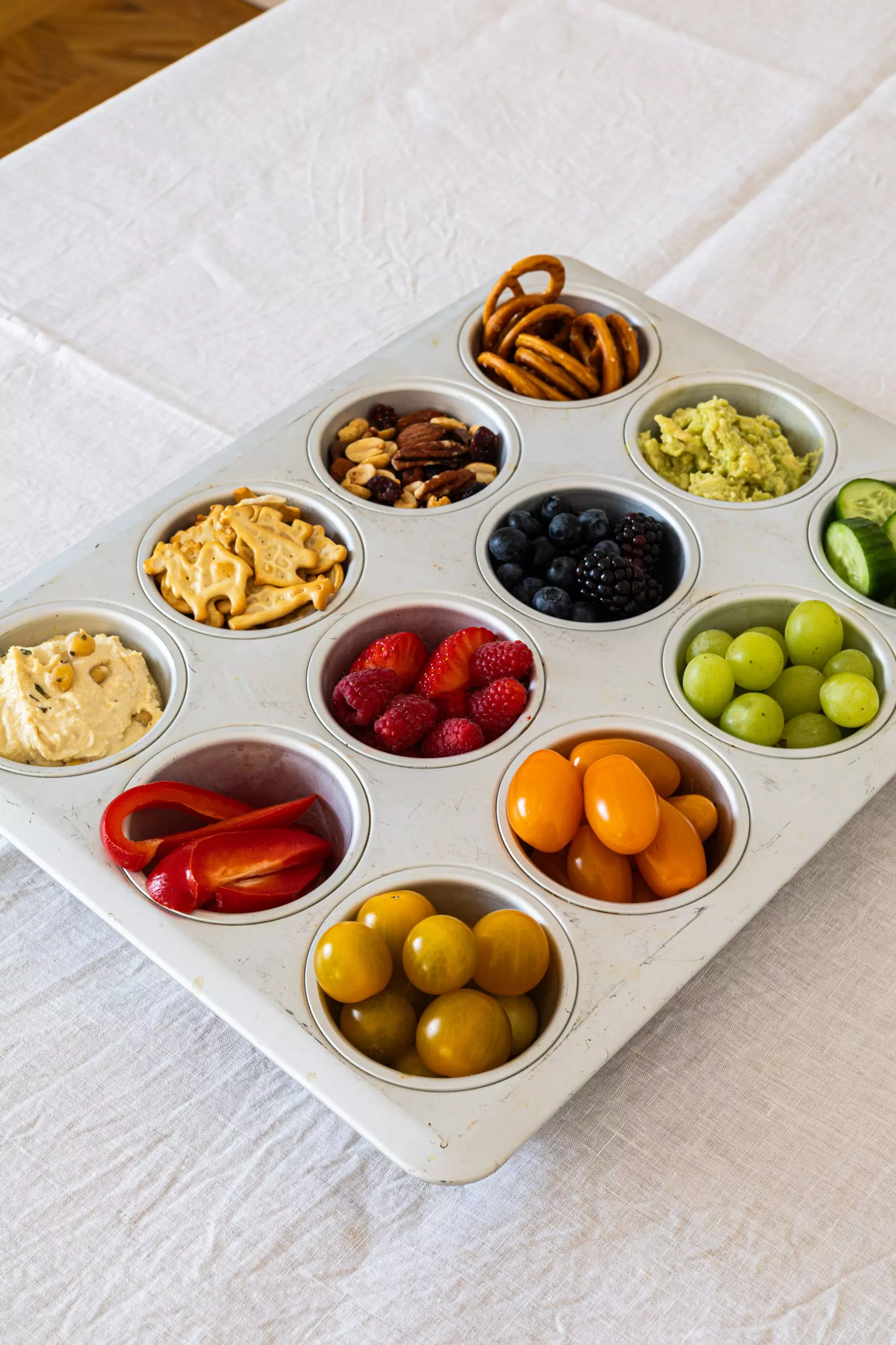In einer Muffinform sind verschiedene Gemüse- und Fruchtportionen übersichtlich und platzsparend für dein nächstes Picknick zu arrangiert. Dies vermeidet Durcheinander und sieht ansprechend aus.