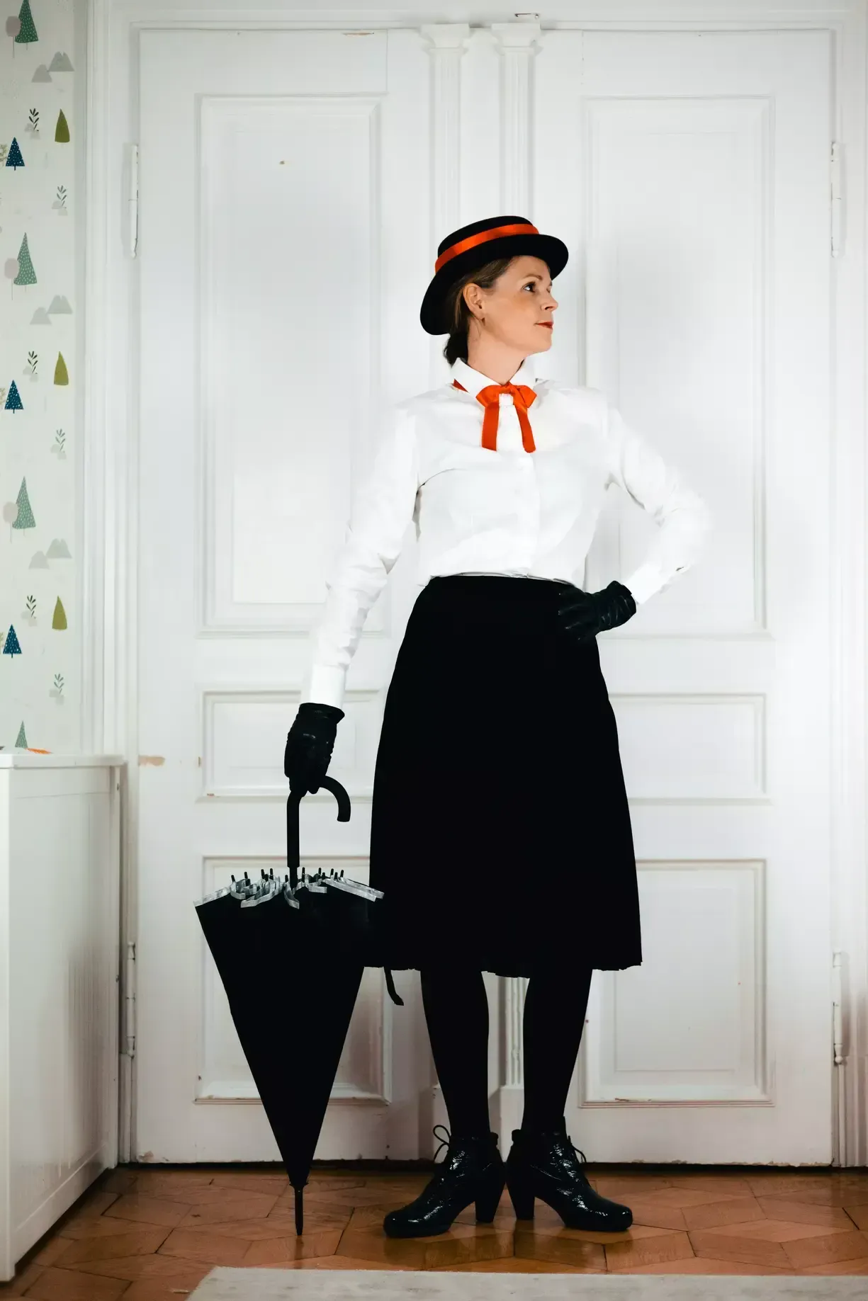 Eine Frau verkleidet als Marry Poppins mit schwarzem Rock, weißer Bluse, Hut, Regenschirm und roter Schleife um den Hals