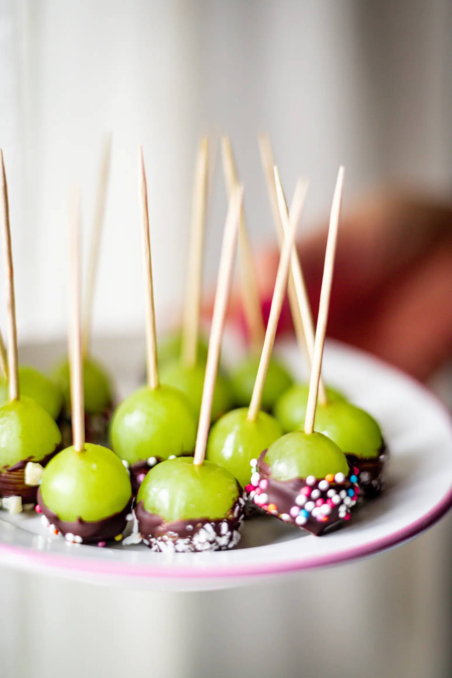 Weintrauben auf Spießen, getaucht in Zartbitter- oder weiße Schokolade und verziert mit Kokosraspeln oder bunten Streuseln, bilden einfache, doch köstliche Snacks für den Kindergeburtstag.