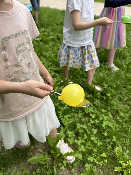 Kinder balancieren Wasserbomben auf Löffeln und versuchen, eine Ziellinie zu erreichen, ohne dass die Bombe herunterfällt. Ein spannendes Rennen, das Geschicklichkeit und Konzentration fordert.